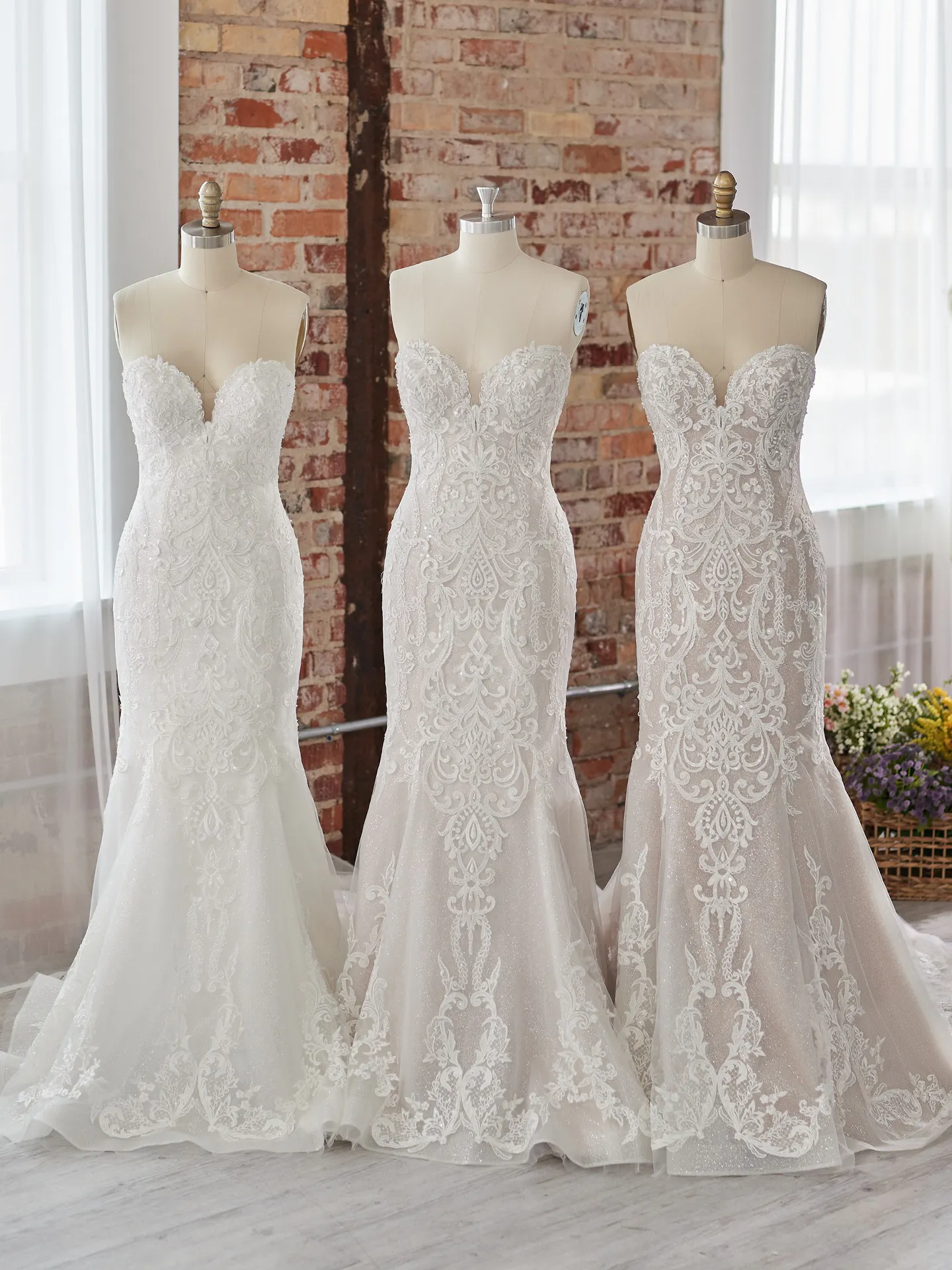 Maggie Sottero Frederique off-the-shoulder bridal gown on mannequins in a brick room.