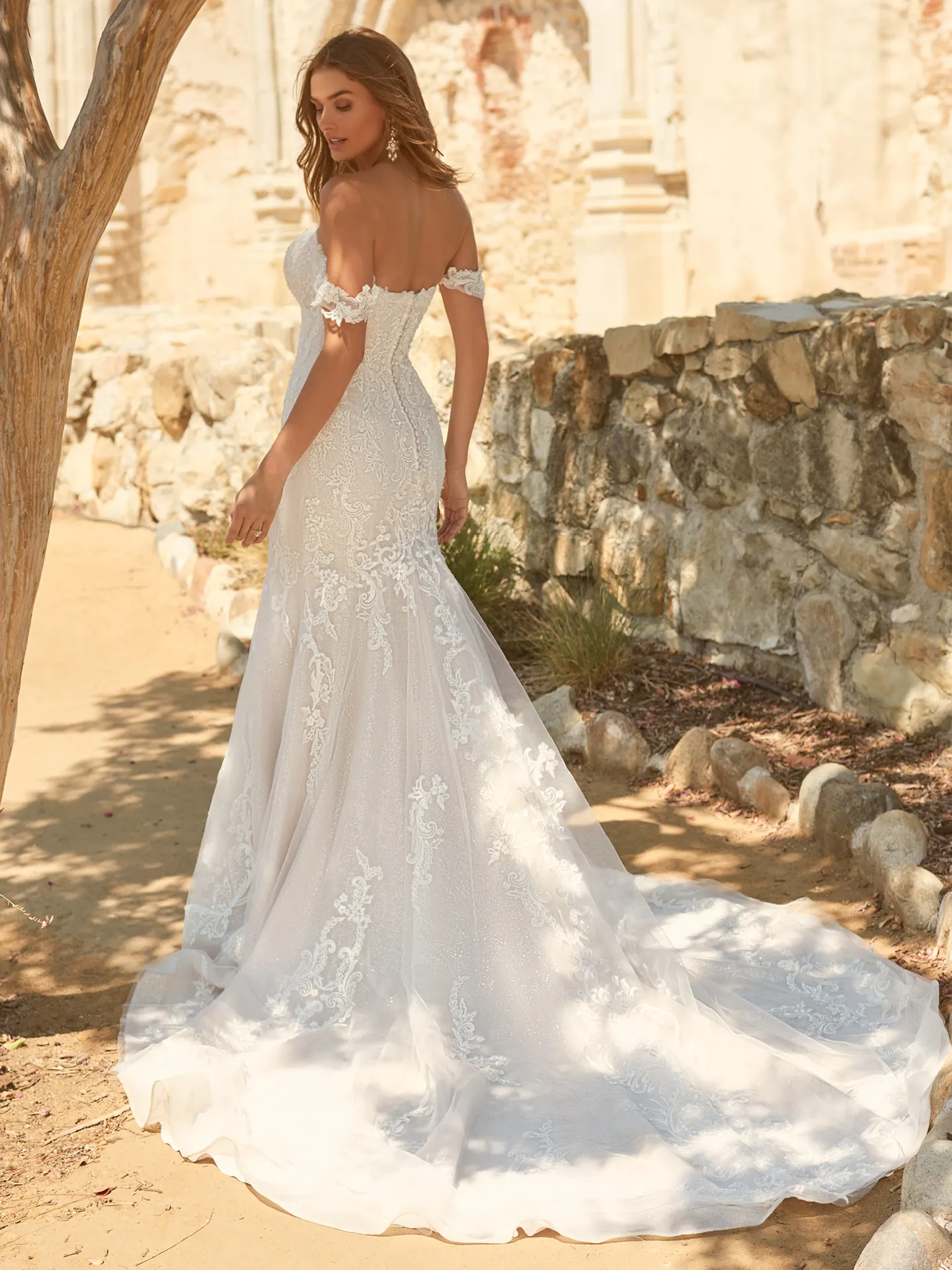 Maggie Sottero Frederique back view elegant off-the-shoulder bridal dress outdoors.