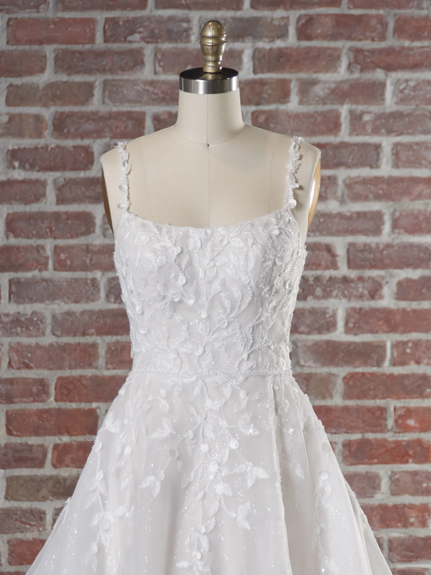 Maggie Sottero dress on mannequin, floral lace, brick wall background