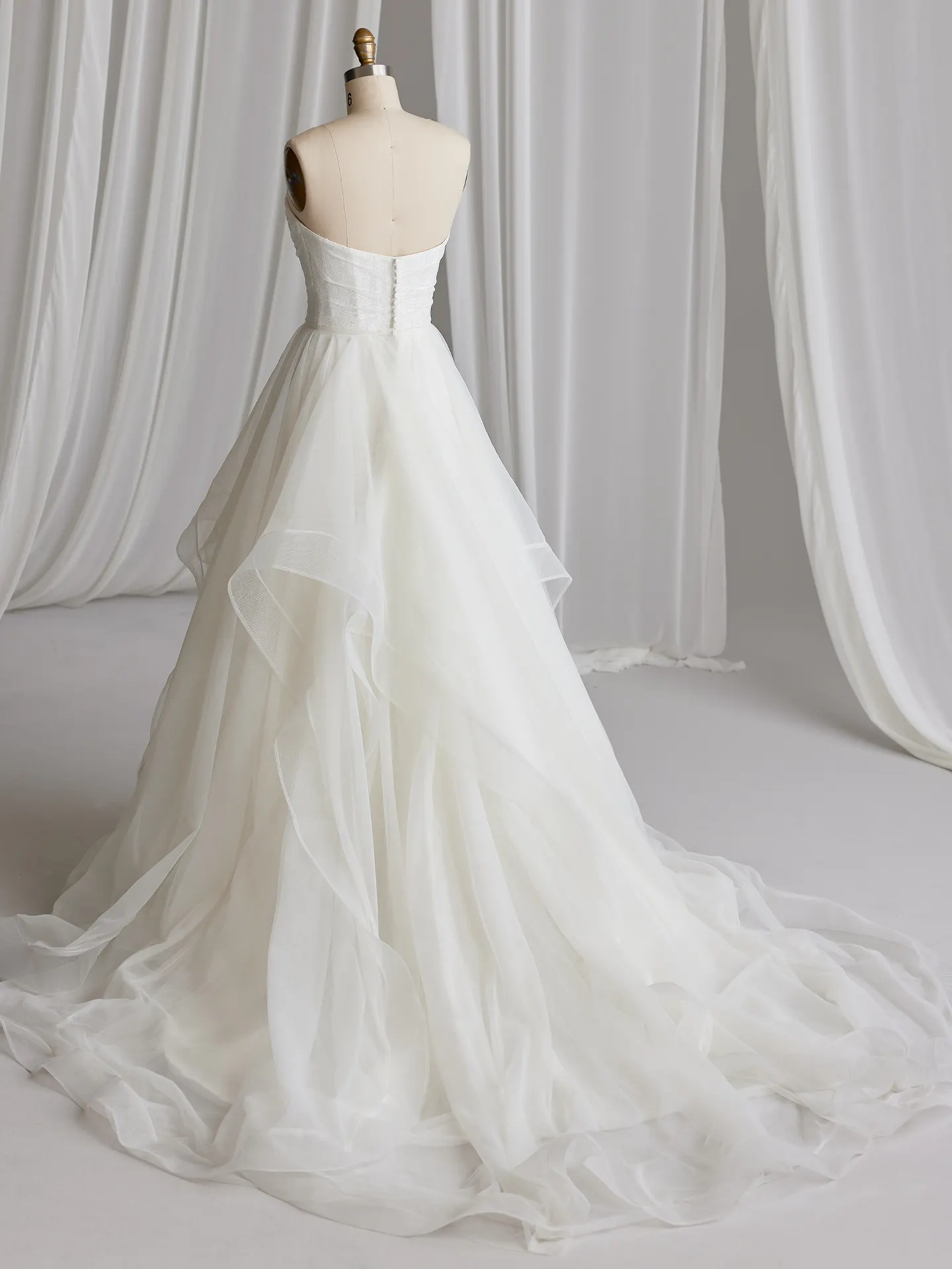 Anniston Lane fit-and-flare bridal gown back view on mannequin in white draped room.