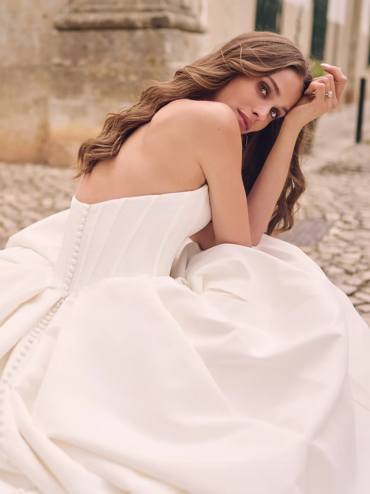 Maggie Sottero Derrick back view, satin bridal gown, sitting on cobblestones.