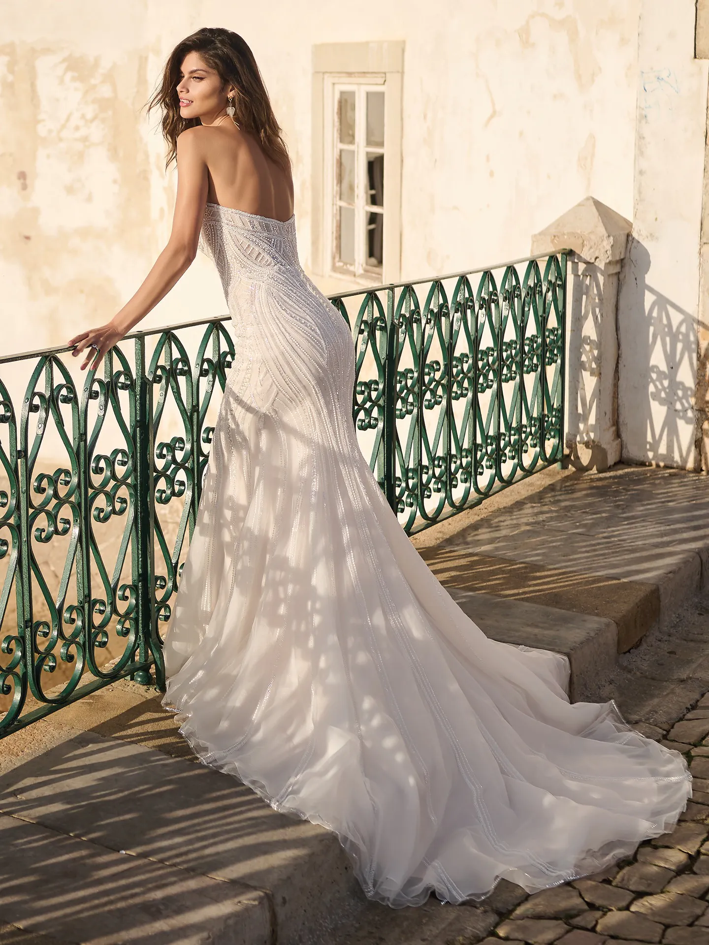 Sottero and Midgley Positano beaded gown back view on stone path with green railing.