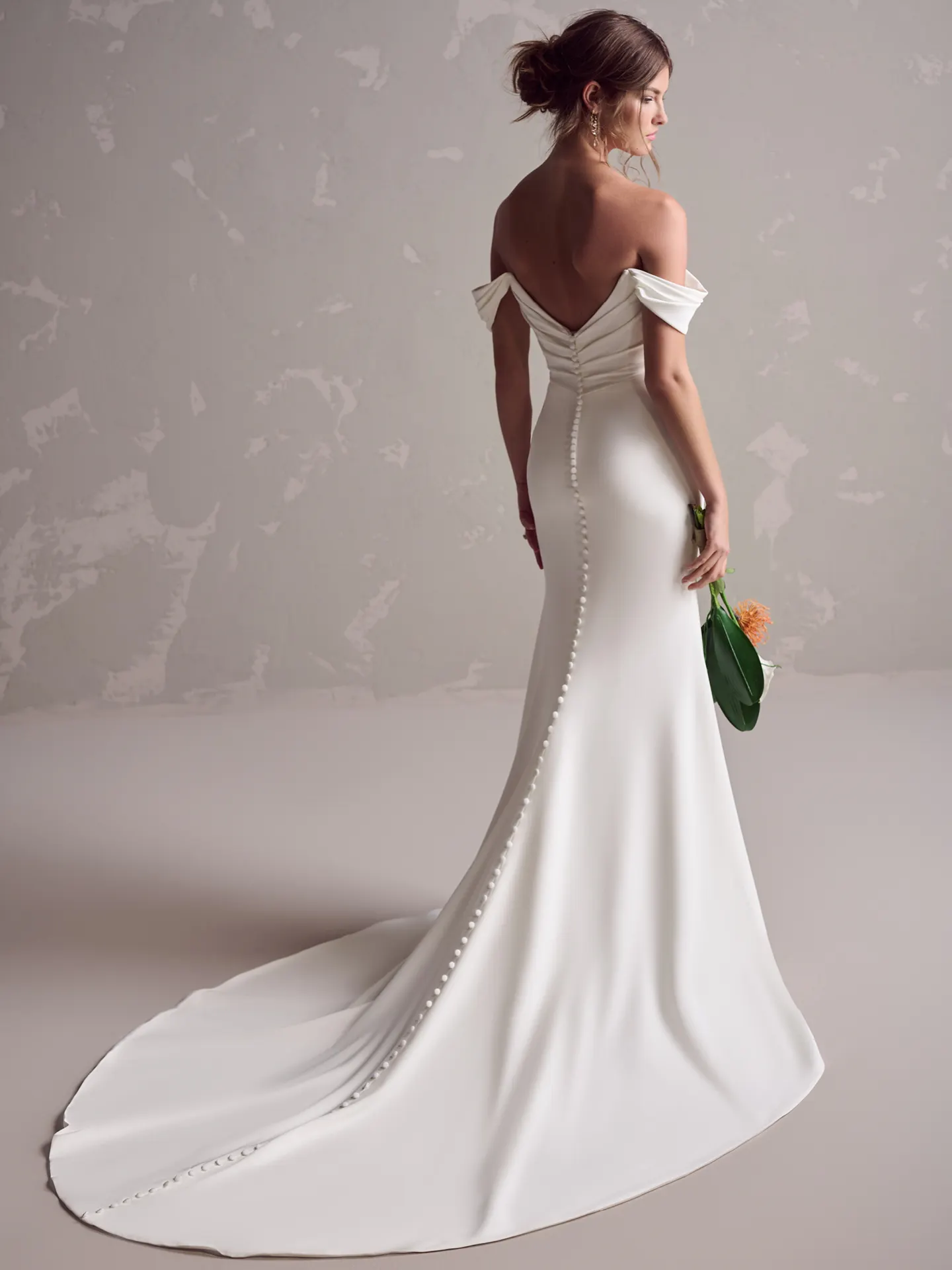 Maggie Sottero crepe wedding dress back view with off-shoulder and button details.