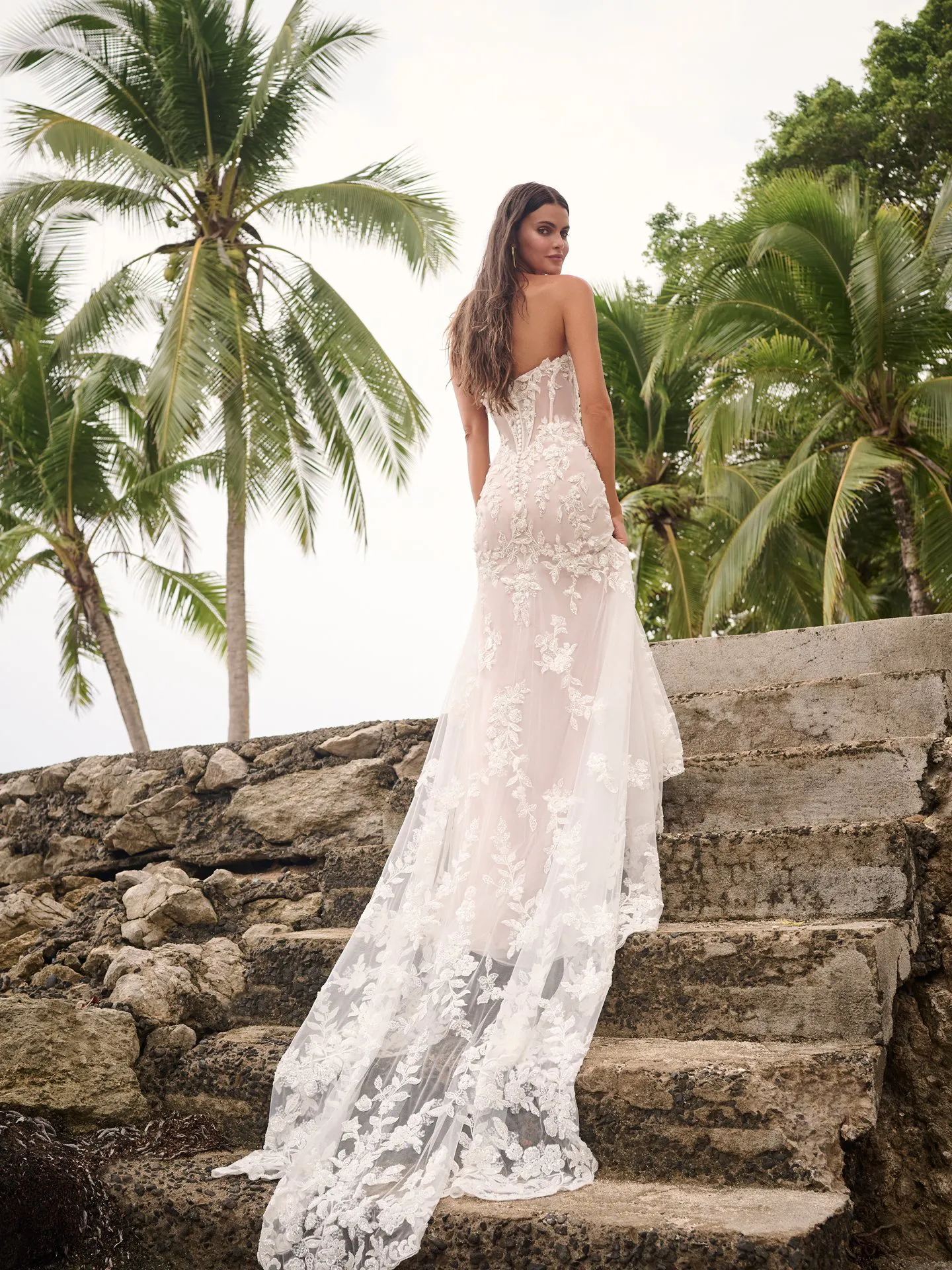 Sottero and Midgley Tanica back view, lace gown on stone steps, palm trees in background.