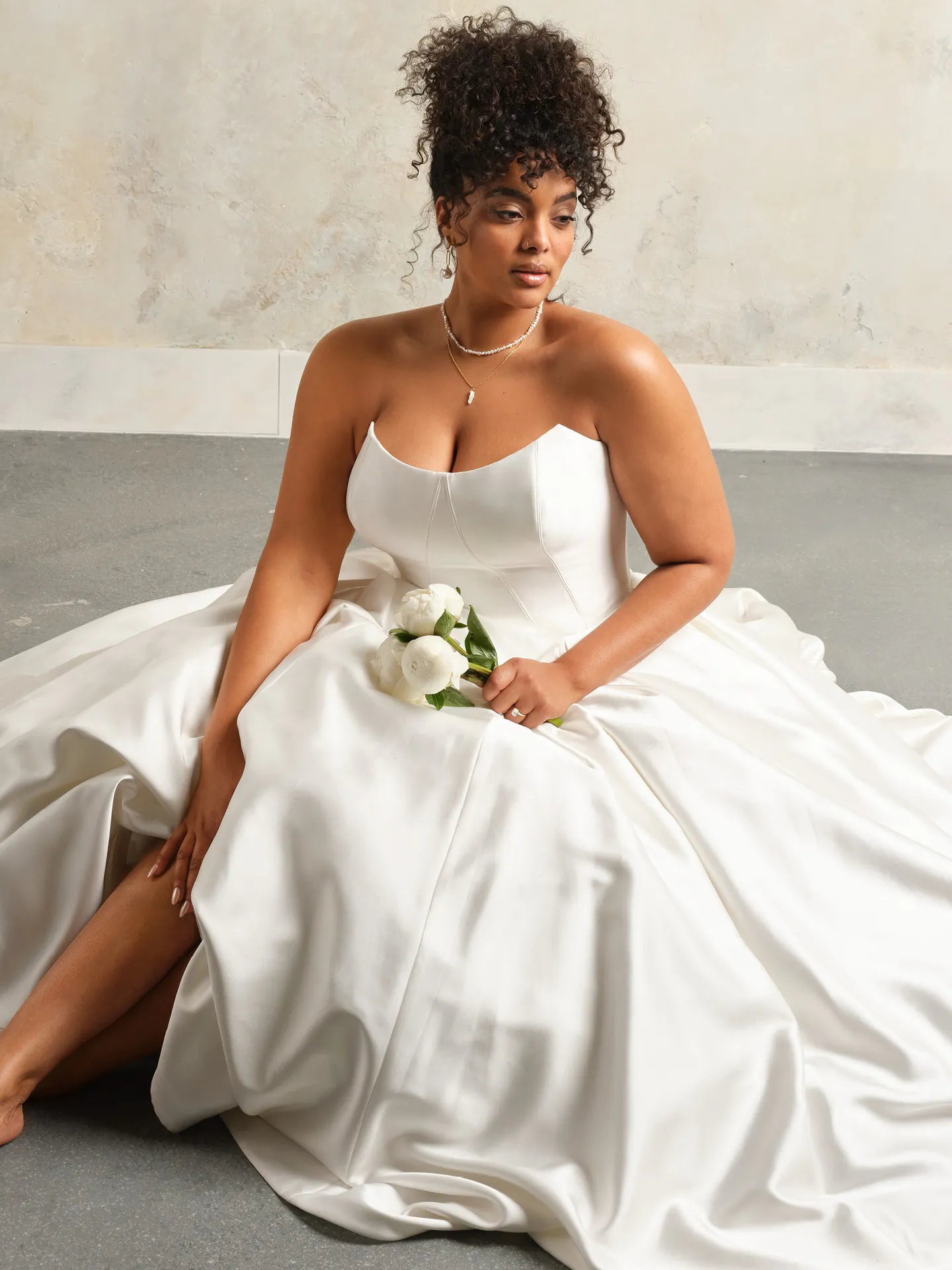 Fortune cat eye bridal dress front view, model seated holding white flowers.