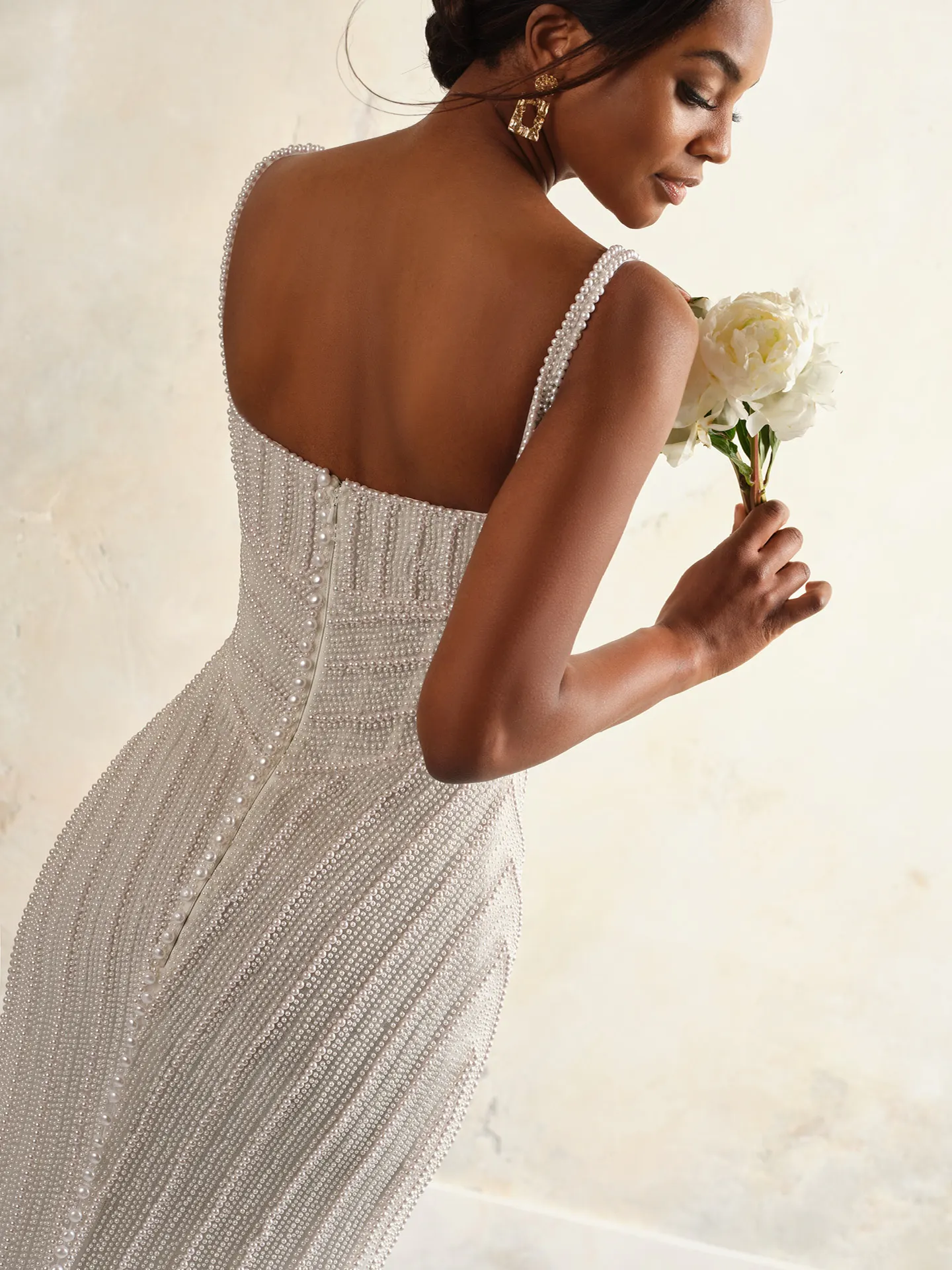 Maggie Sottero Danica back view pearl wedding gown with basque waist, model holding flowers.