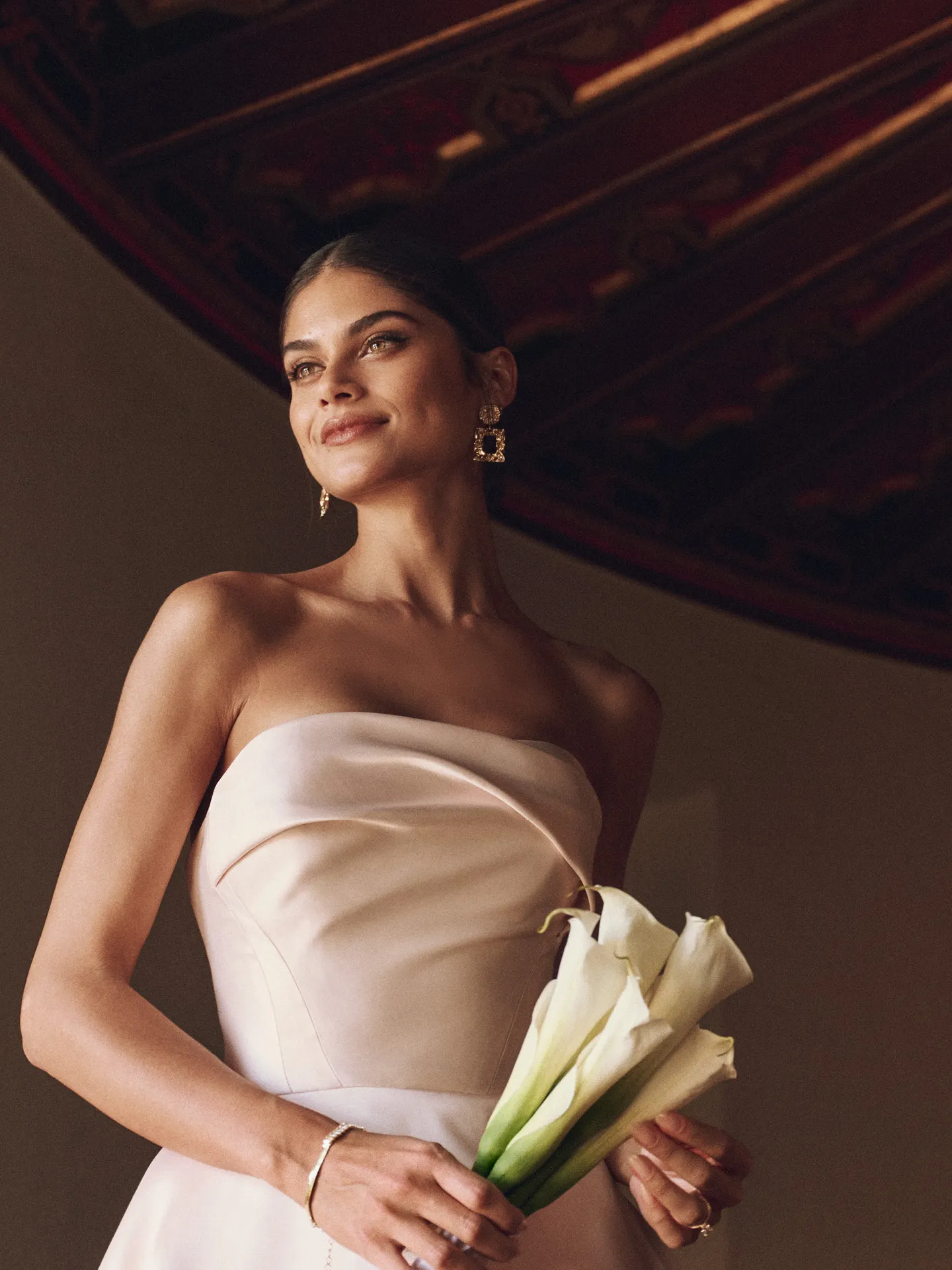 Strapless asymmetrical Faro draped Mikado bridal gown close-up, holding lilies.