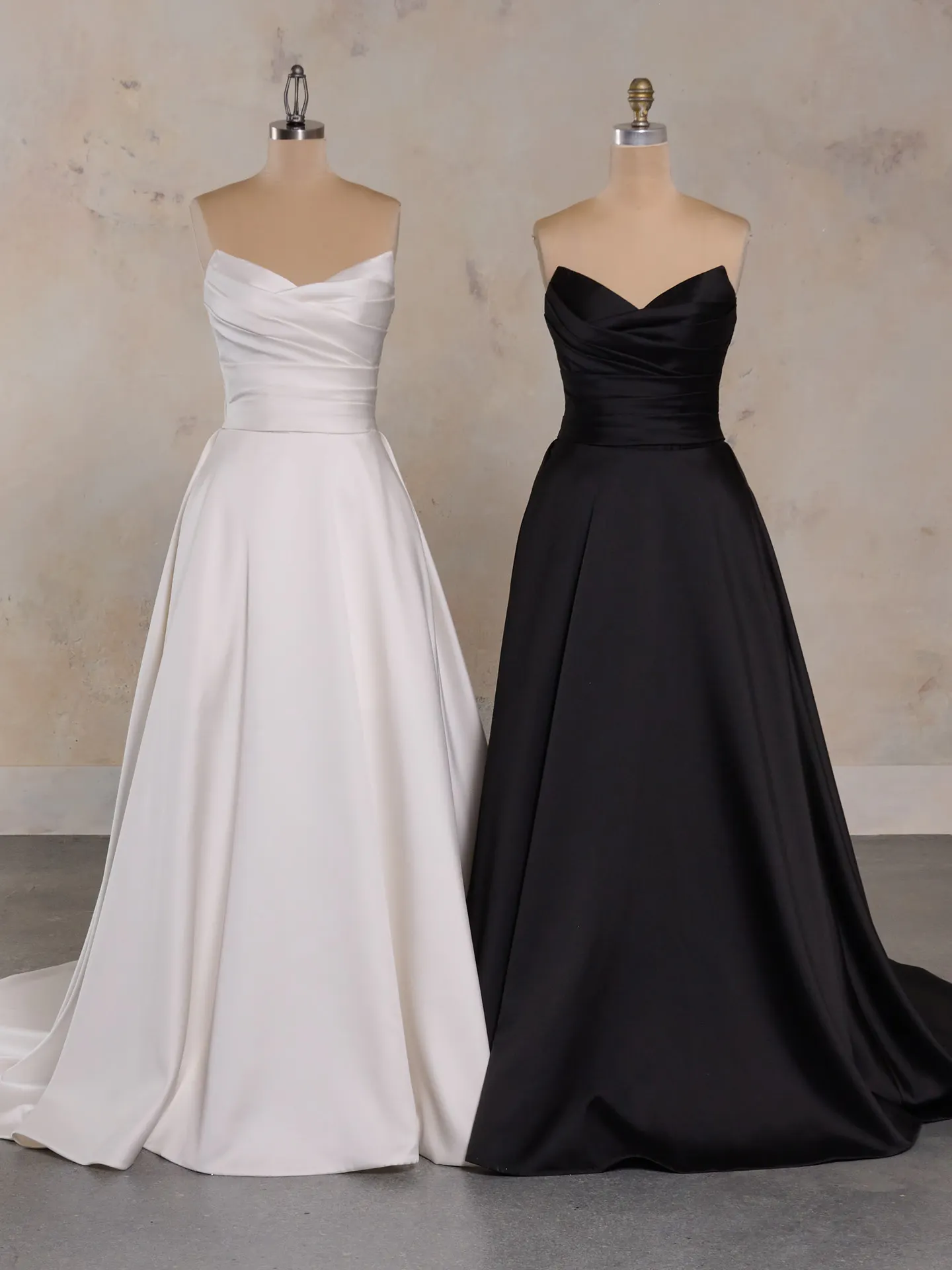 White and black strapless floor-length dresses on mannequins in a studio setting.