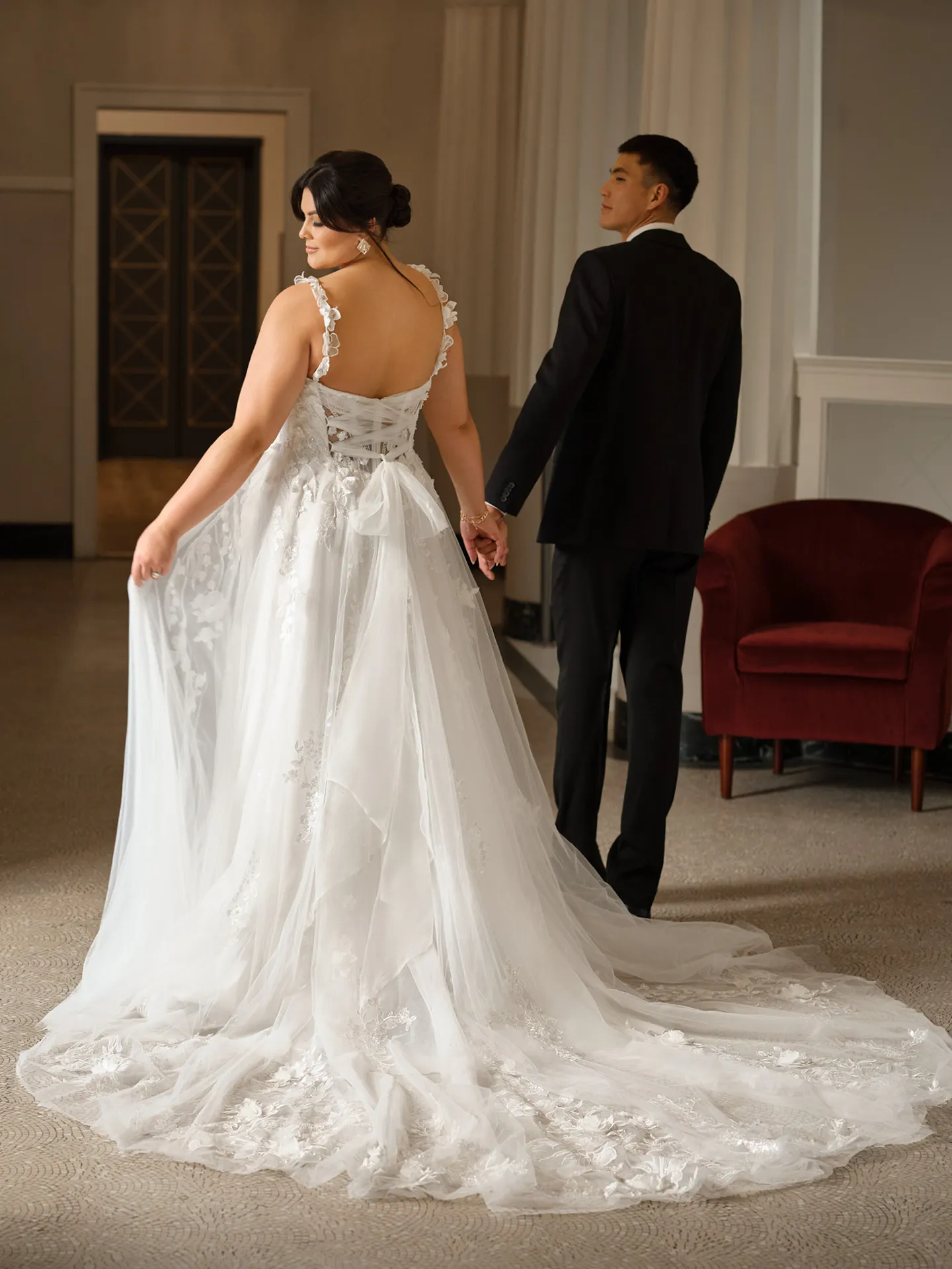 Rebecca Ingram Wicklow back view shows floral lace side-slit bridal dress in an elegant room.