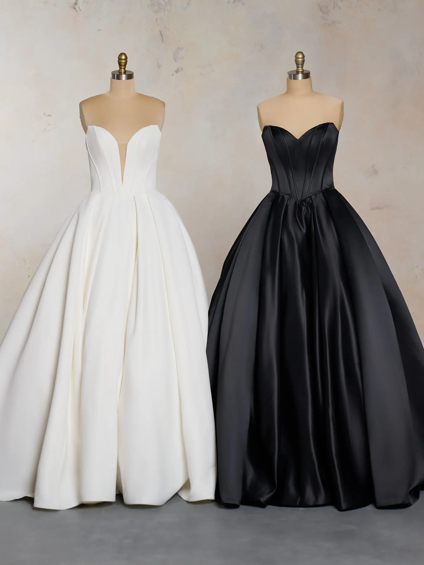 White and black satin ballgowns on mannequins against a neutral background.