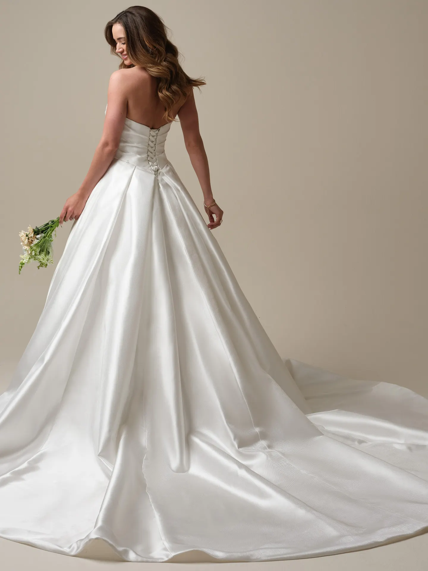 Maggie Sottero Aubrielle back view satin ball gown with corset and floral bouquet