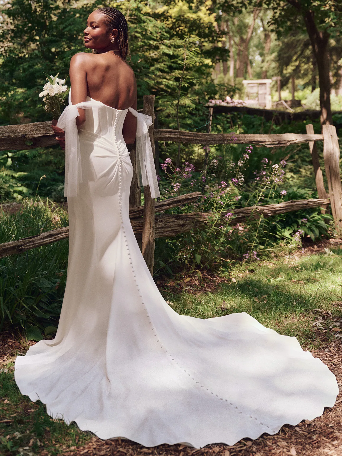 Maggie Sottero Jace back view, exposed boning, crepe sheath wedding dress in a garden setting.