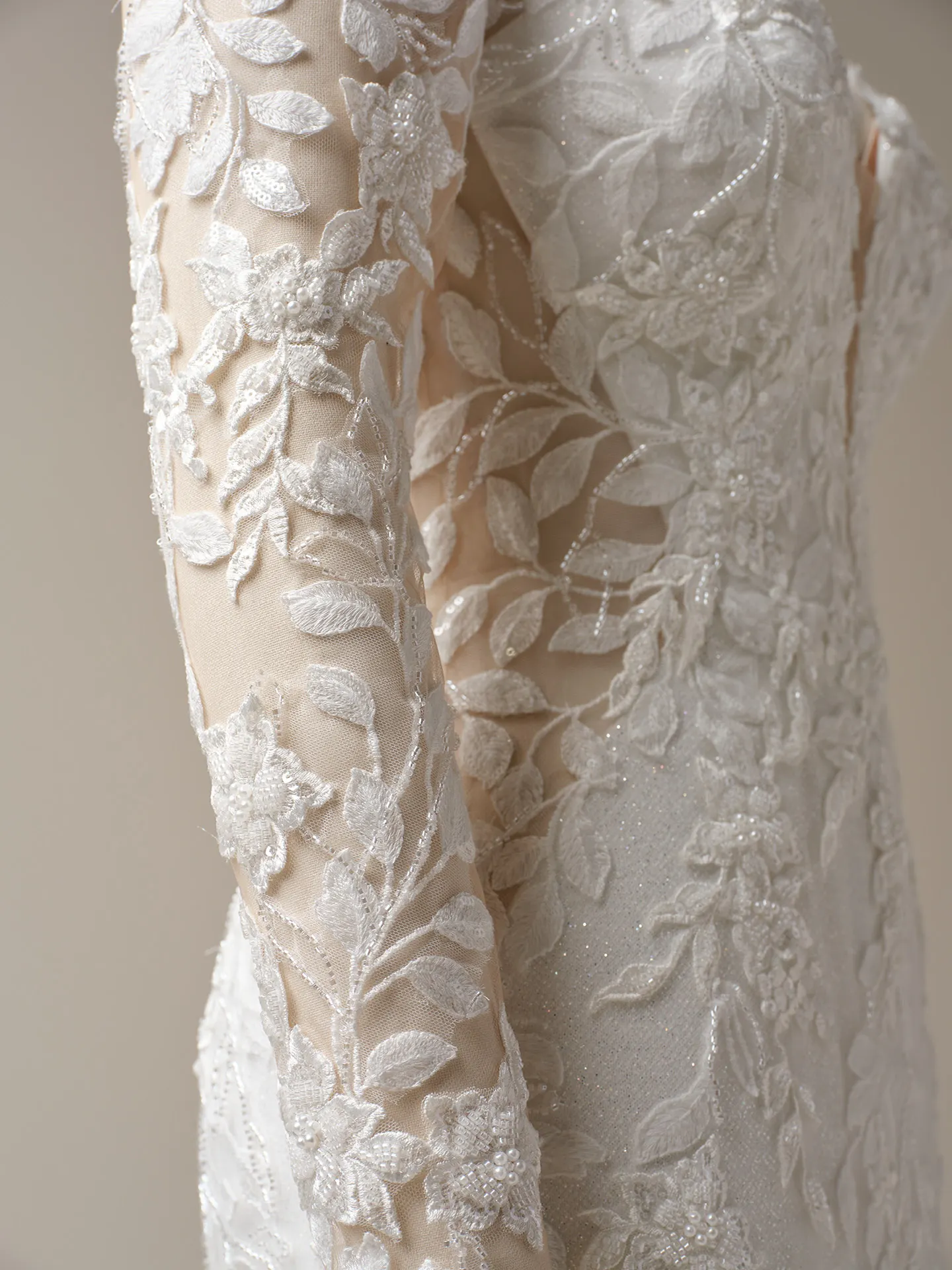 Keegan by Maggie Sottero closeup. Glittering lace and floral details on sheer sleeve.