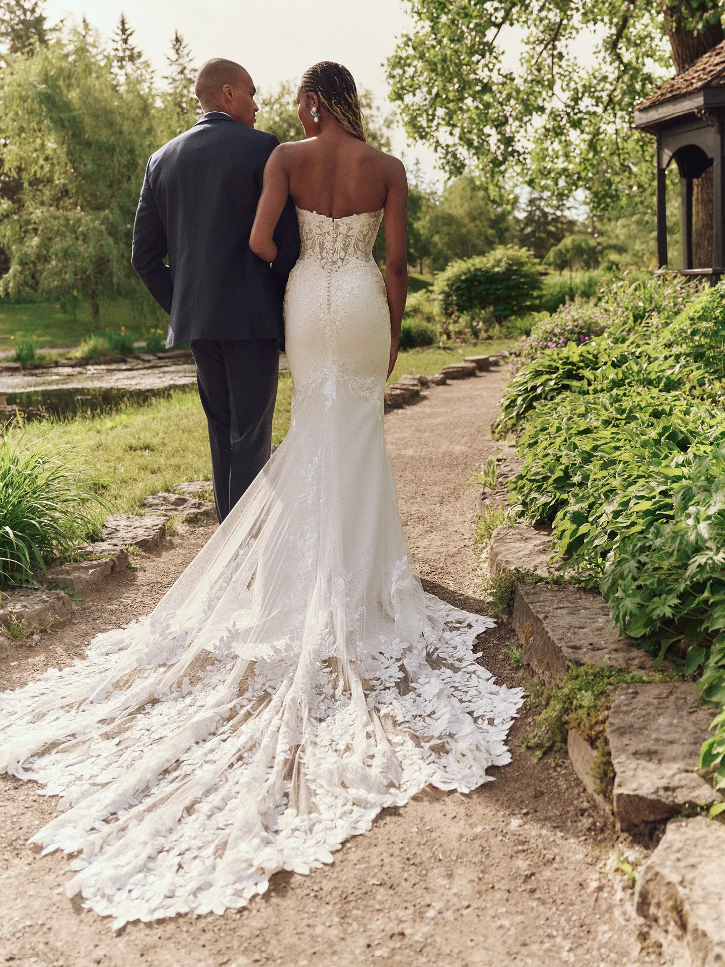 Maggie Sottero Yara back view lace train sheath dress in garden path setting.