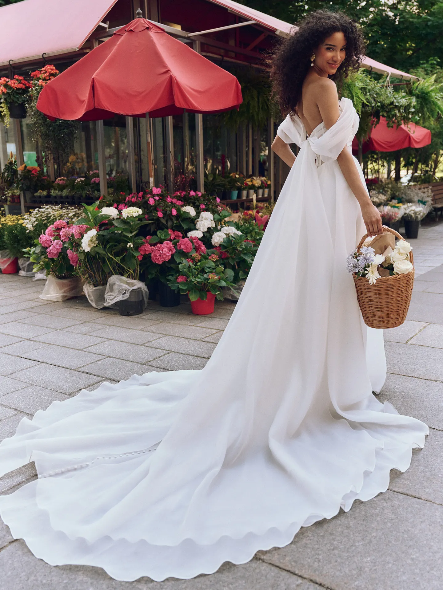 Rebecca Ingram Sunny back view, off-the-shoulder gown with train near flower shop.