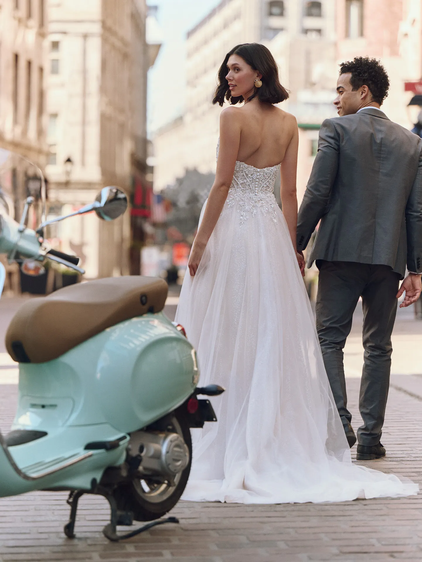 Maggie Sottero Yvette back view in city street with a blue scooter in foreground