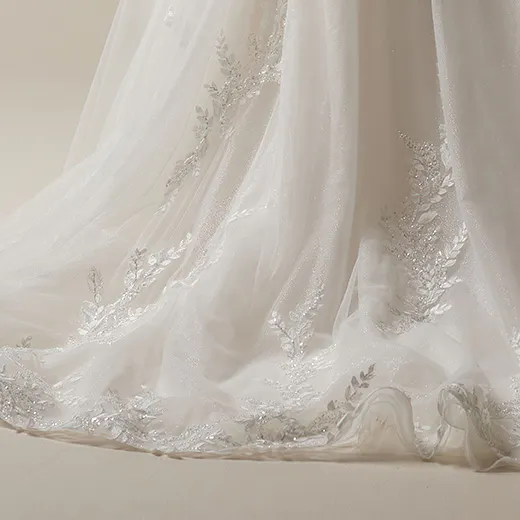 Maggie Sottero Rita detail of off-the-shoulder beaded A-line bridal gown hem with leaf embroidery.