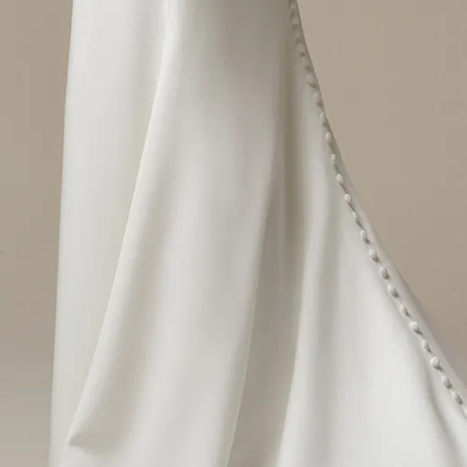Maggie Sottero Kailani. Side view of crepe cowl dress with buttons.