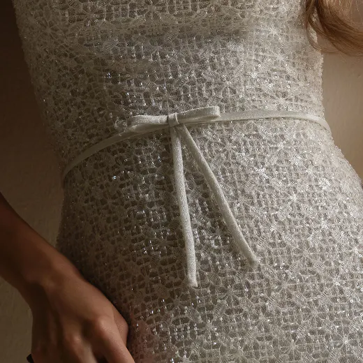 Maggie Sottero glittering sheath bridal gown with bow detail, close up view.