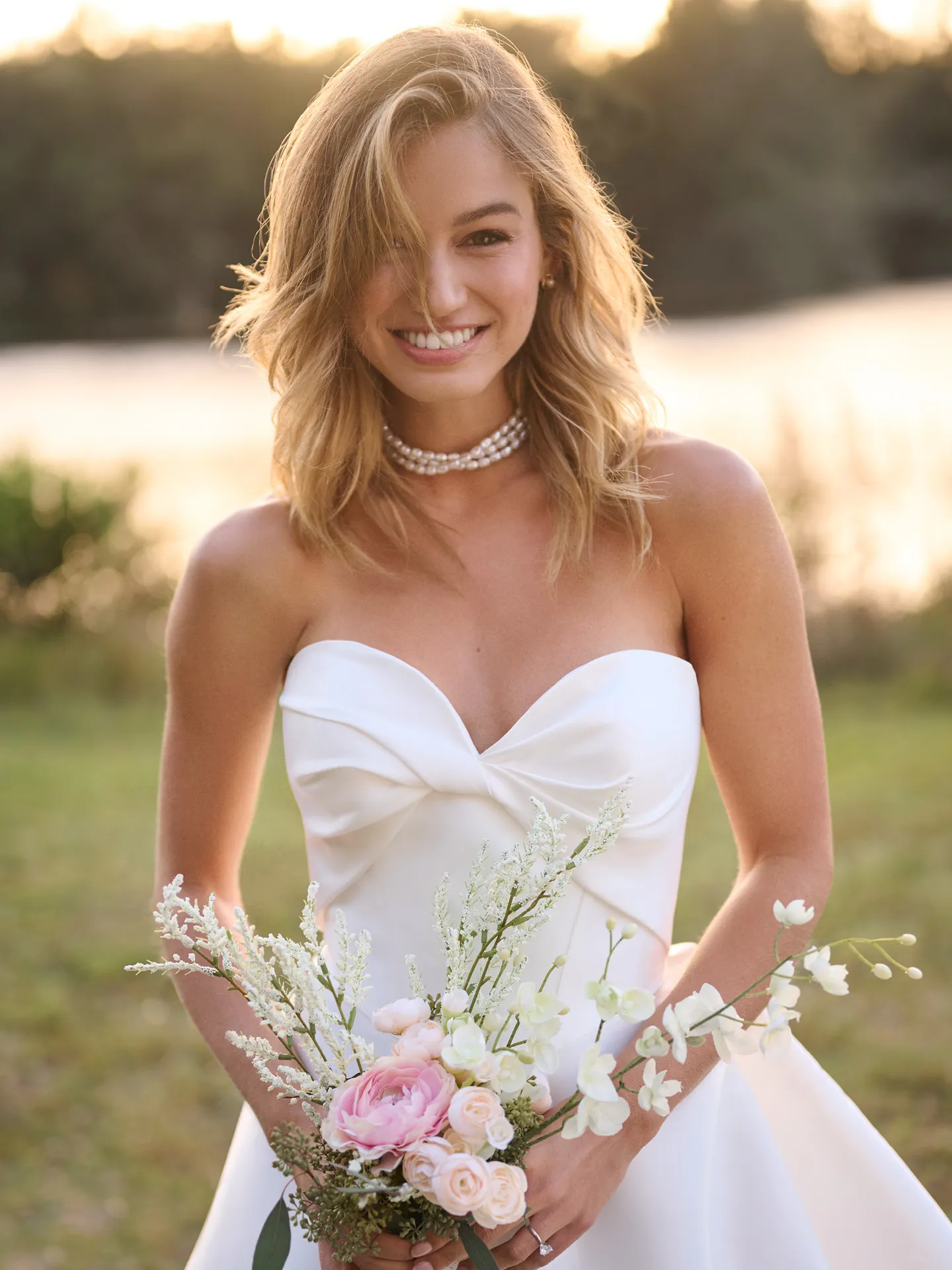 Rebecca Ingram Brooke front view, strapless A-line bridal gown, outdoors with bouquet.