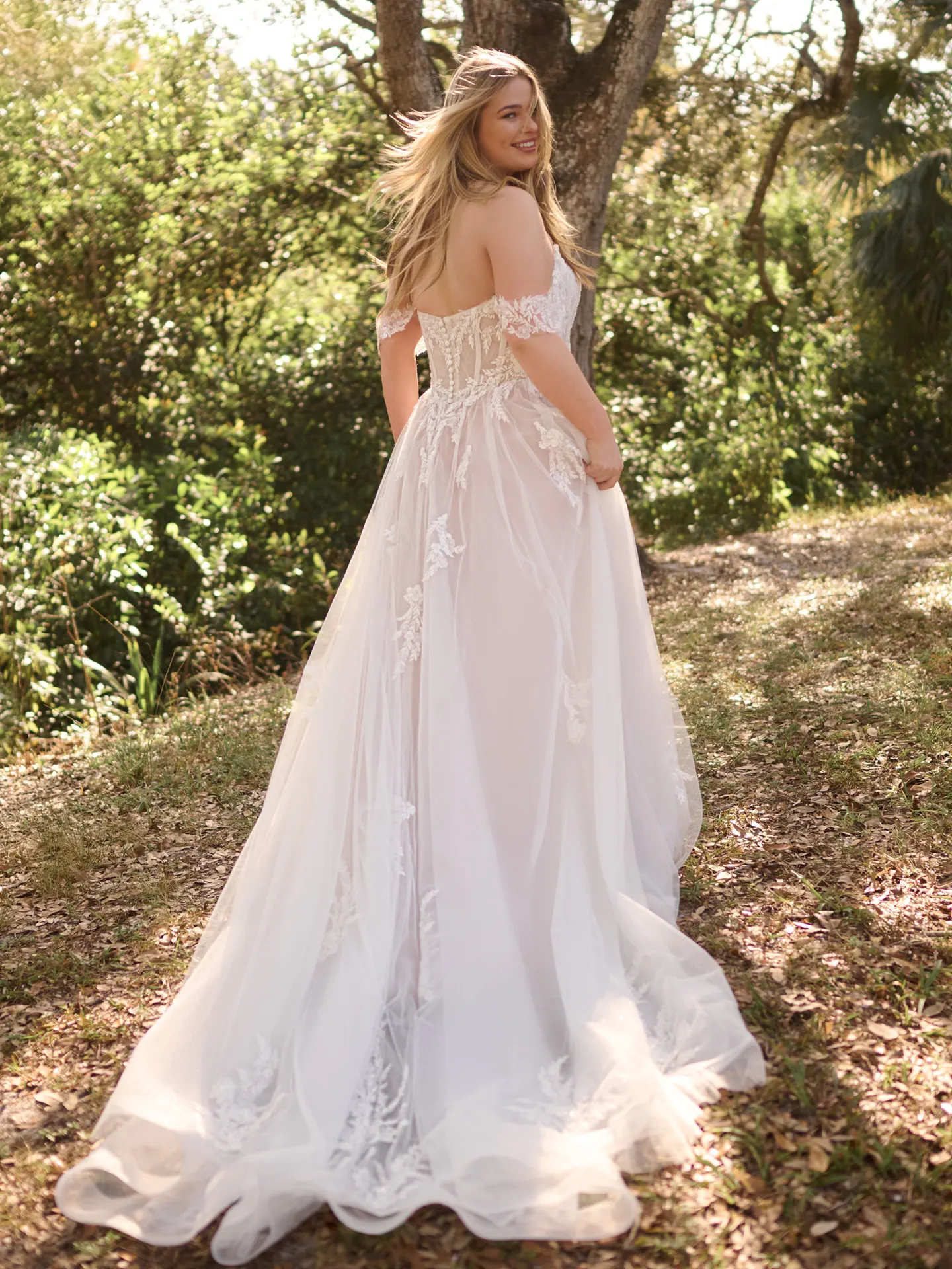Rebecca Ingram Victoria back view A-line bridal gown with floral details in a forest setting.