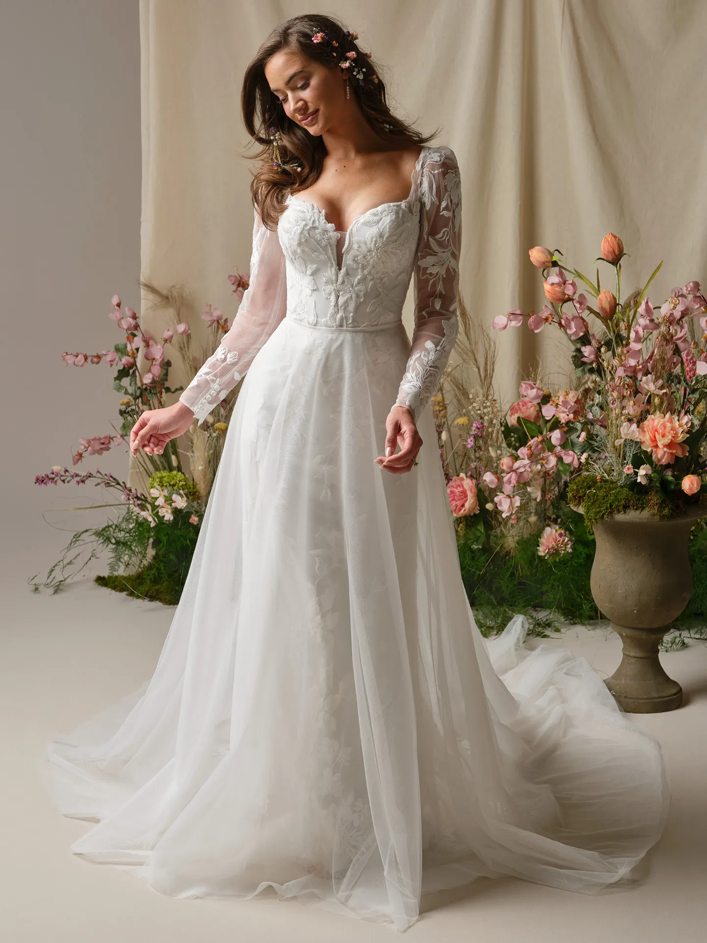 Rebecca Ingram Aubra, front view, fit-and-flare lace wedding dress, floral backdrop.