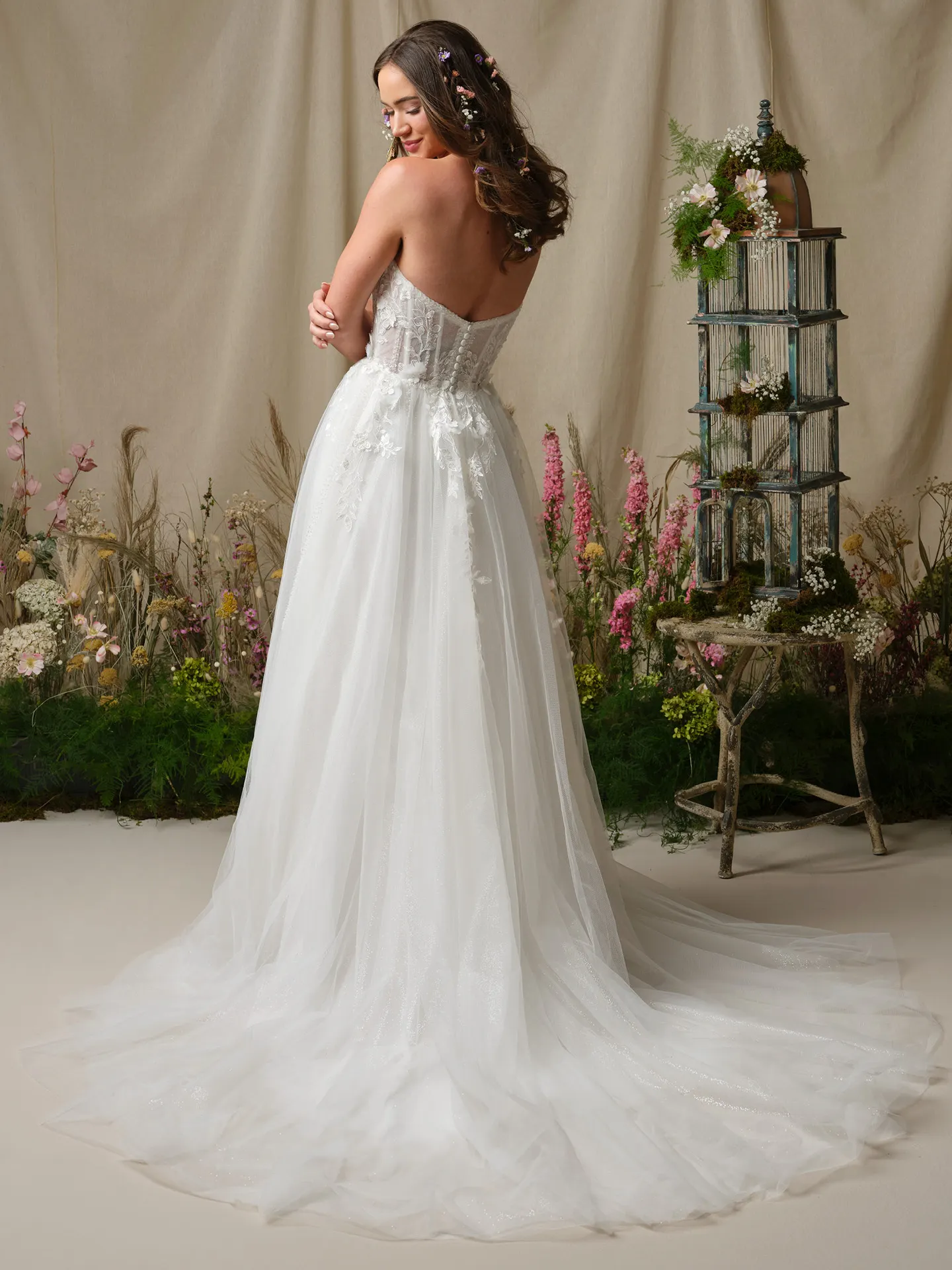 Rebecca Ingram Nora back view, floral decorated hair, A-line wedding dress in garden setting