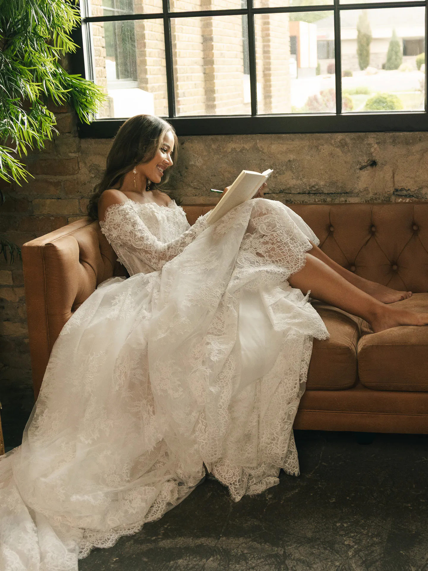 Maggie Sottero Kitaro lace ballgown, side view, model sitting on couch in rustic room.