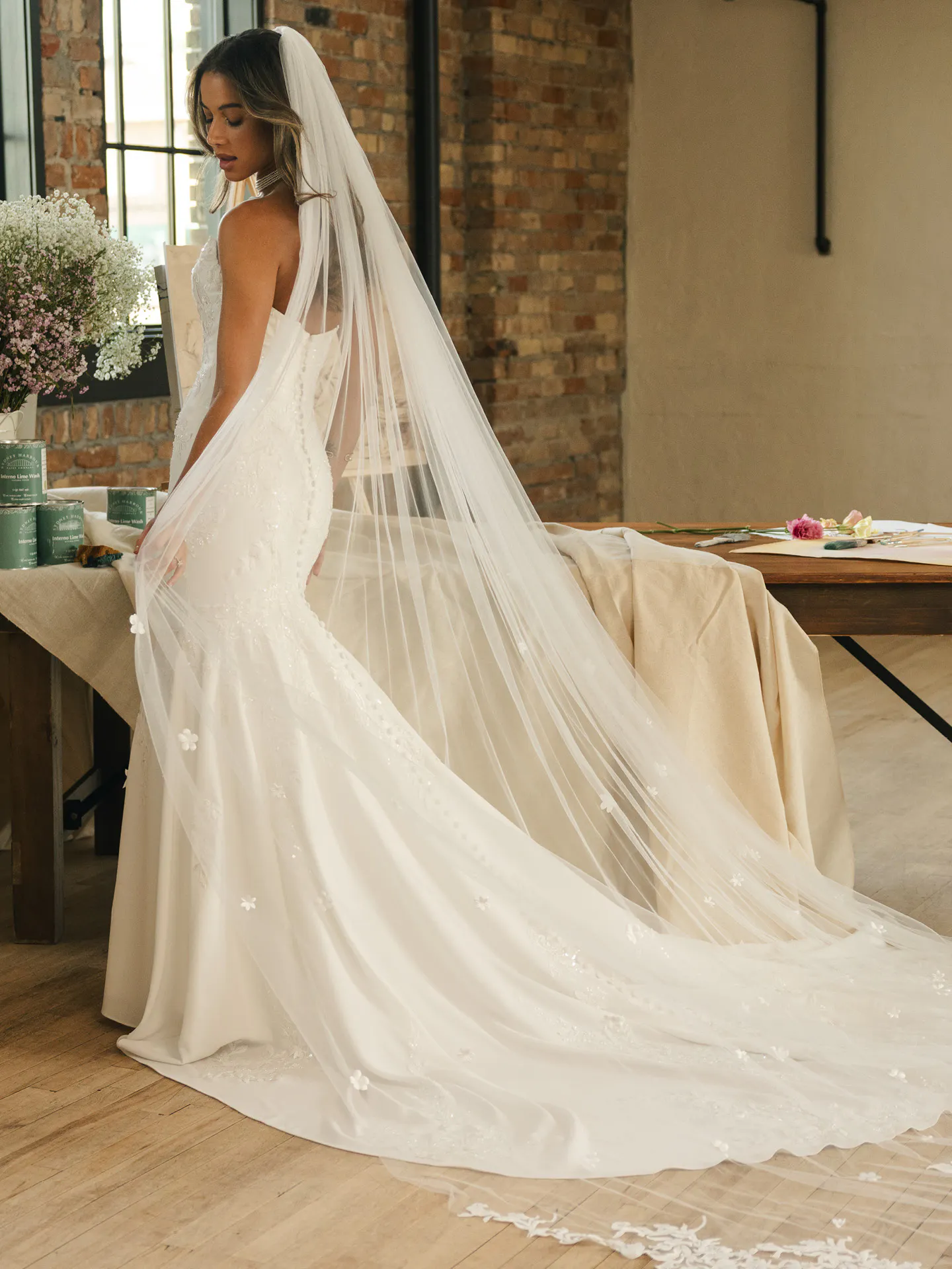 Maggie Sottero Thera fit-and-flare wedding dress side view with long veil, brick wall background.