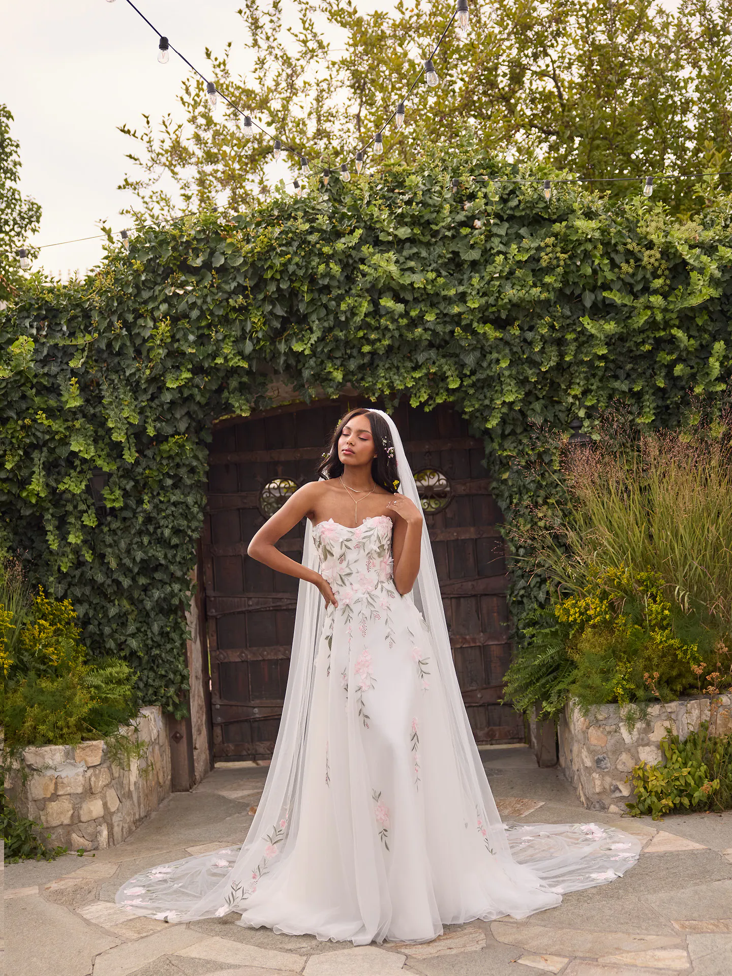 Rebecca Ingram Blossom, front view, strapless floral lace A-line wedding dress in garden setting.