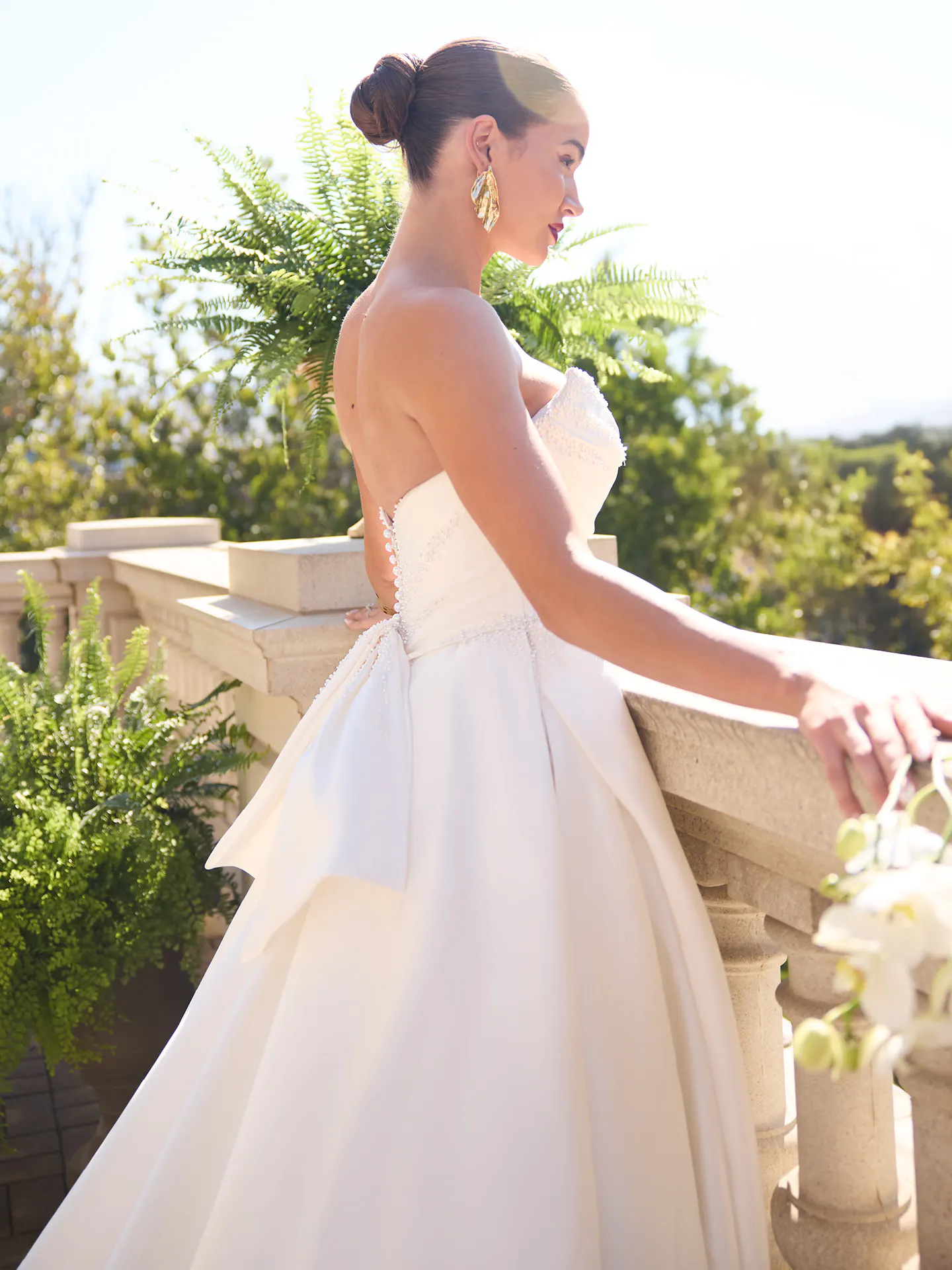 Sottero and Midgley Kincaid, side view satin ballgown with bow on terrace.